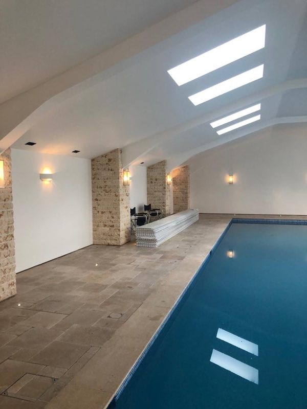 Indoor pool beside a stone floor, with roof lights and wall lights along the room