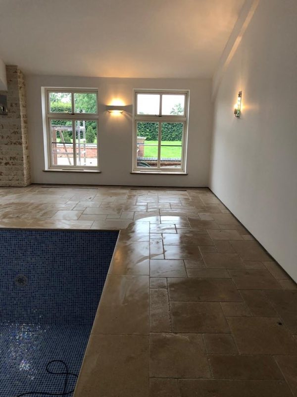 Corner of a mosaic-tiled pool and the stone floor in front of garden windows