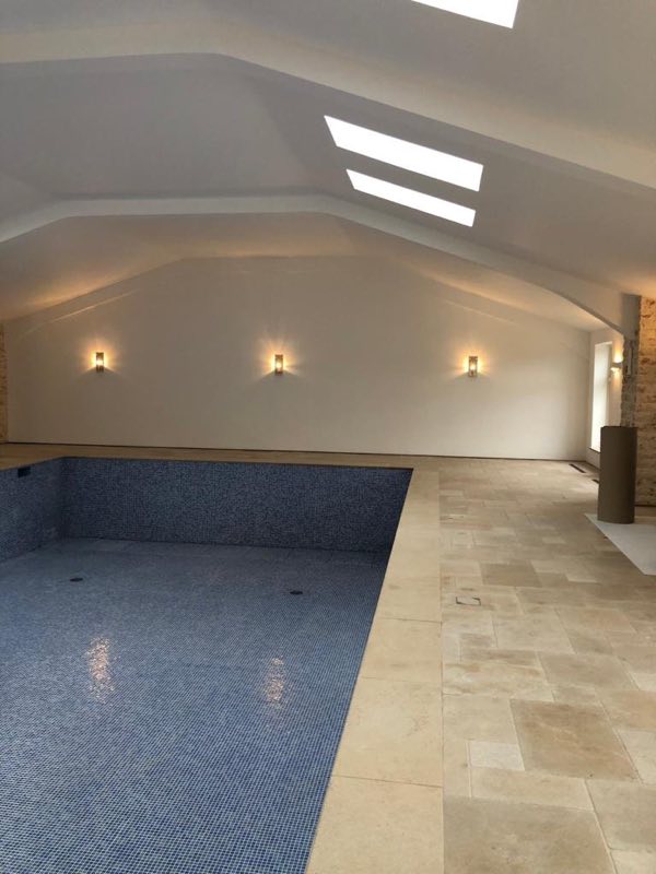 Indoor pool shell tiled in blue mosaic under roof lights, before filling
