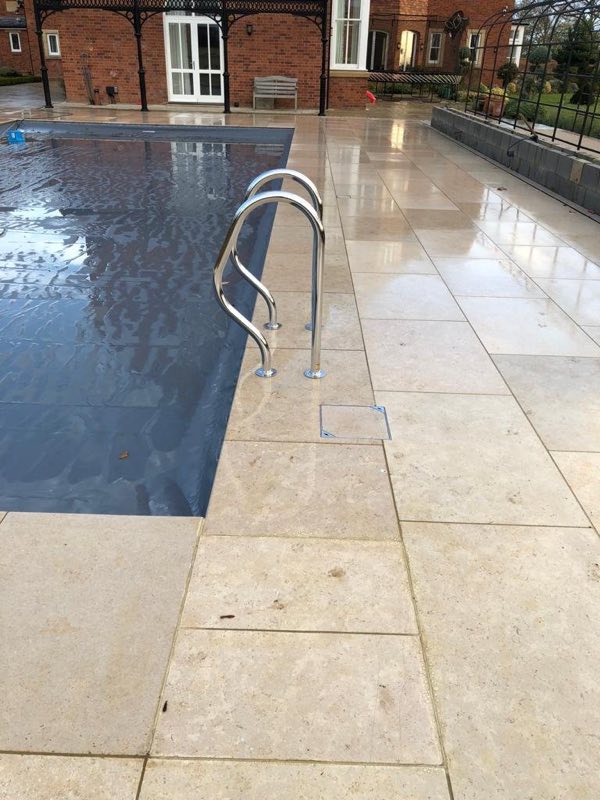 Outdoor pool with a stainless-steel ladder and wide stone paving