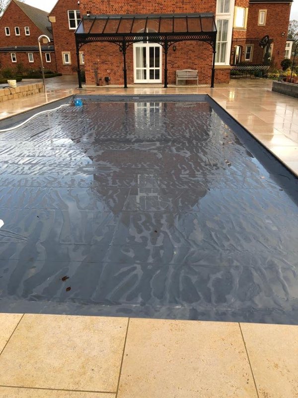 Outdoor pool with a stone surround in front of a brick house