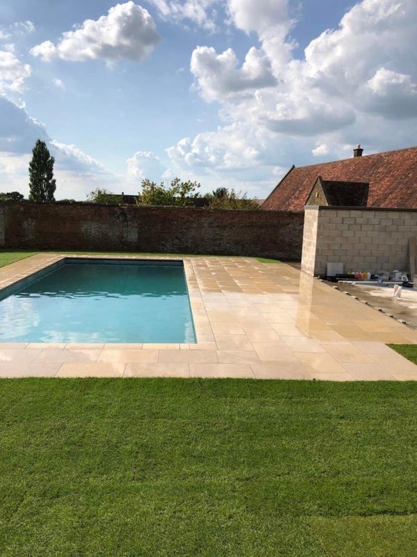 Outdoor pool set in a lawn beside a garden wall and stone outbuilding