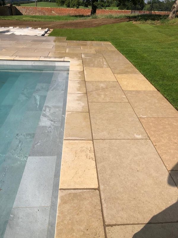 Stone coping and paving beside the shallow end of an outdoor pool