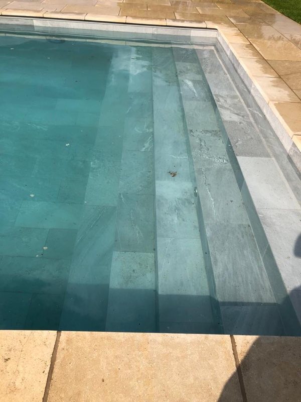 Clear water over tiled steps running the width of an outdoor pool