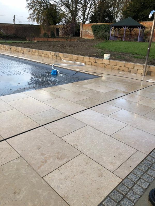 Stone paving around an outdoor pool, with a gazebo in the garden