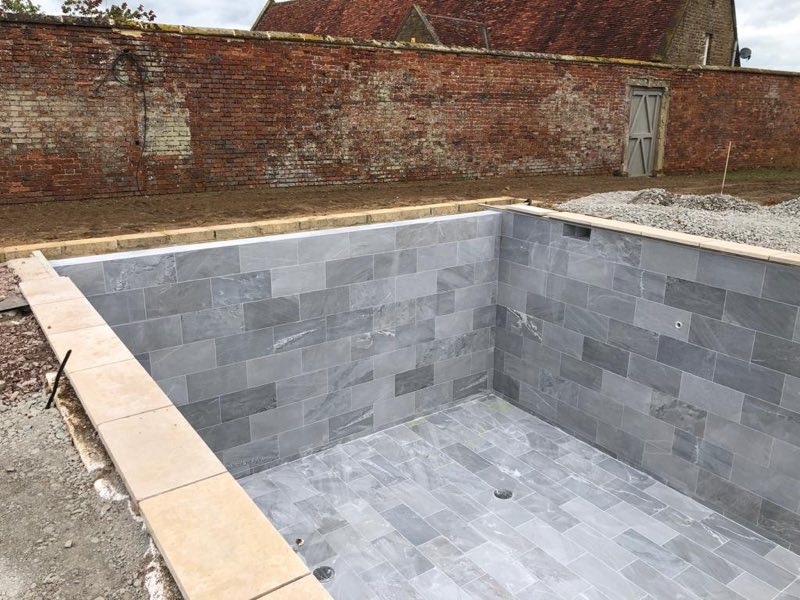 Pool shell tiled in grey stone-effect tiles inside a walled garden