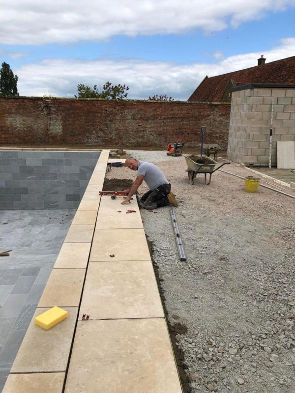 Coping stones being laid along the edge of a tiled pool