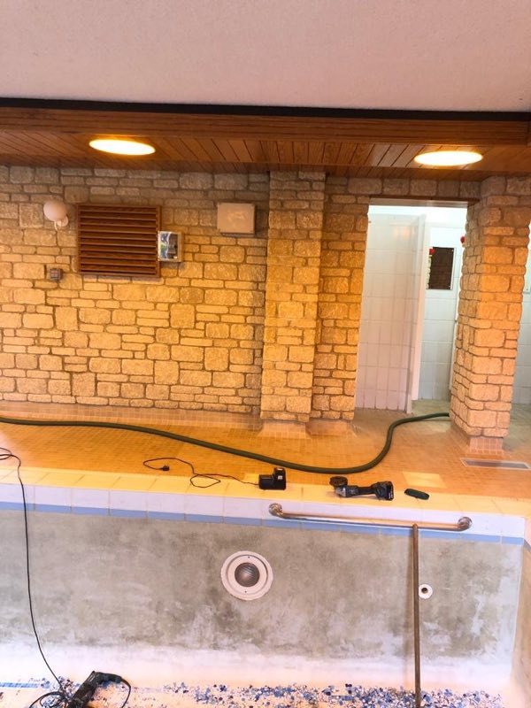 Drained indoor pool in a stone-walled room, with the walls stripped back
