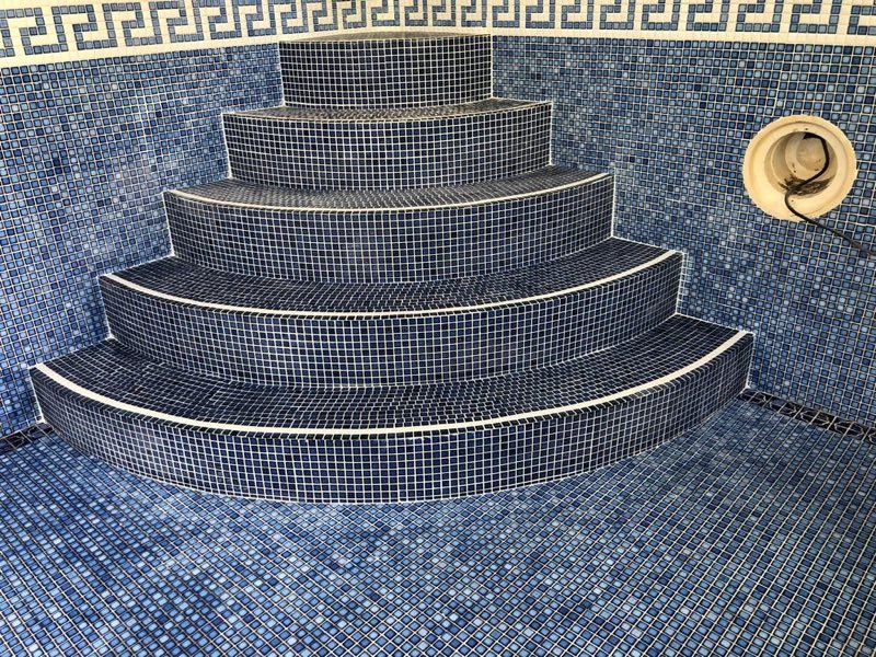 Curved pool steps tiled in blue mosaic with a Greek key border
