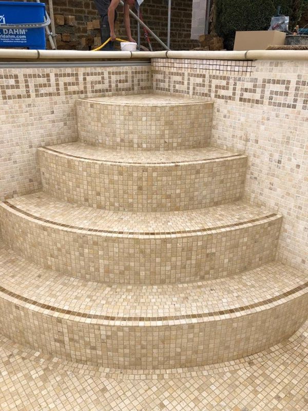 Curved pool steps in cream mosaic with a Greek key border